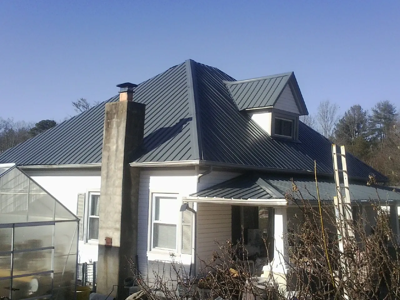 Dark blue standing seam metal roof on a white farmhouse with dormer — Slate & Tile Roof Repair by Roofing Brothers in Cypress