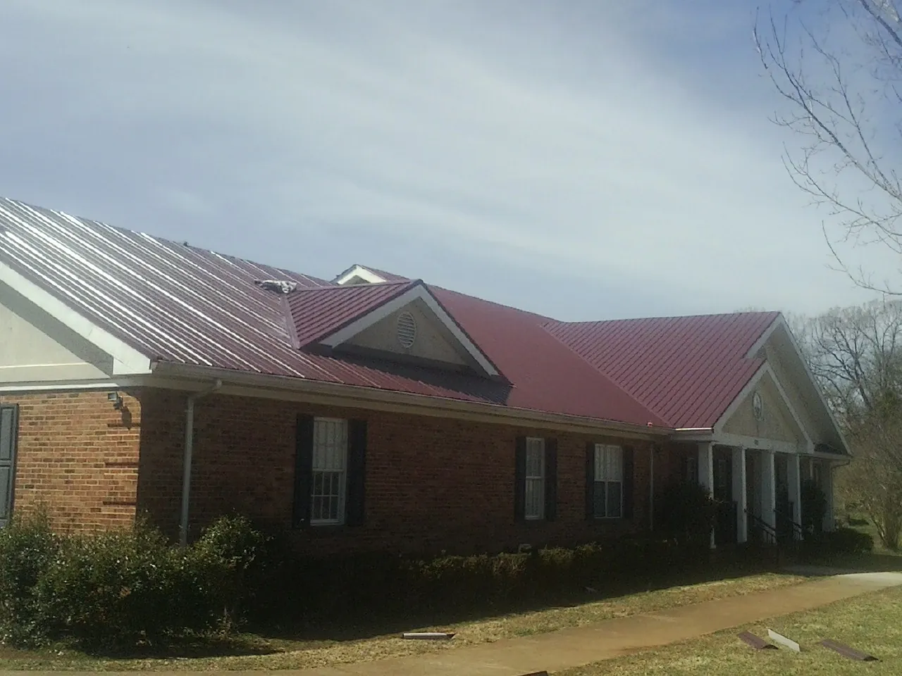 Red metal roof with gabled entries on a long brick building, from a Hail Damage Roof Repair job in Cypress