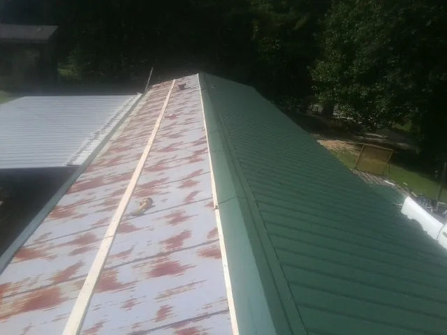 Old rusted panels beside newly installed green metal roofing — Wind Damage Roof Repair by Roofing Brothers in Cypress