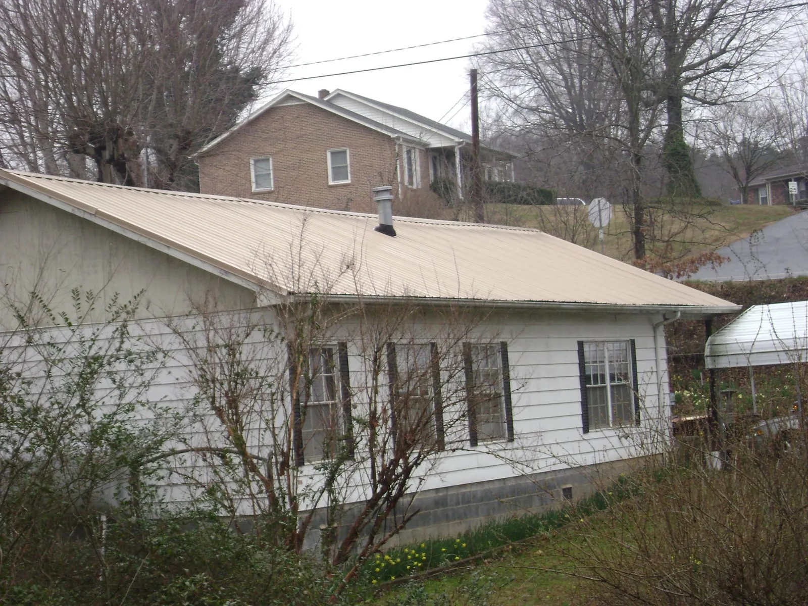 Tan metal roof on a white sided house set into a hillside — Commercial Roofing by Roofing Brothers in Cypress