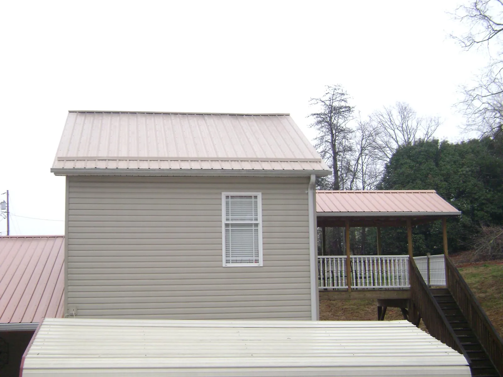 Tan metal roofs on a two story addition and attached porch, from a Roof Replacement job in Cypress